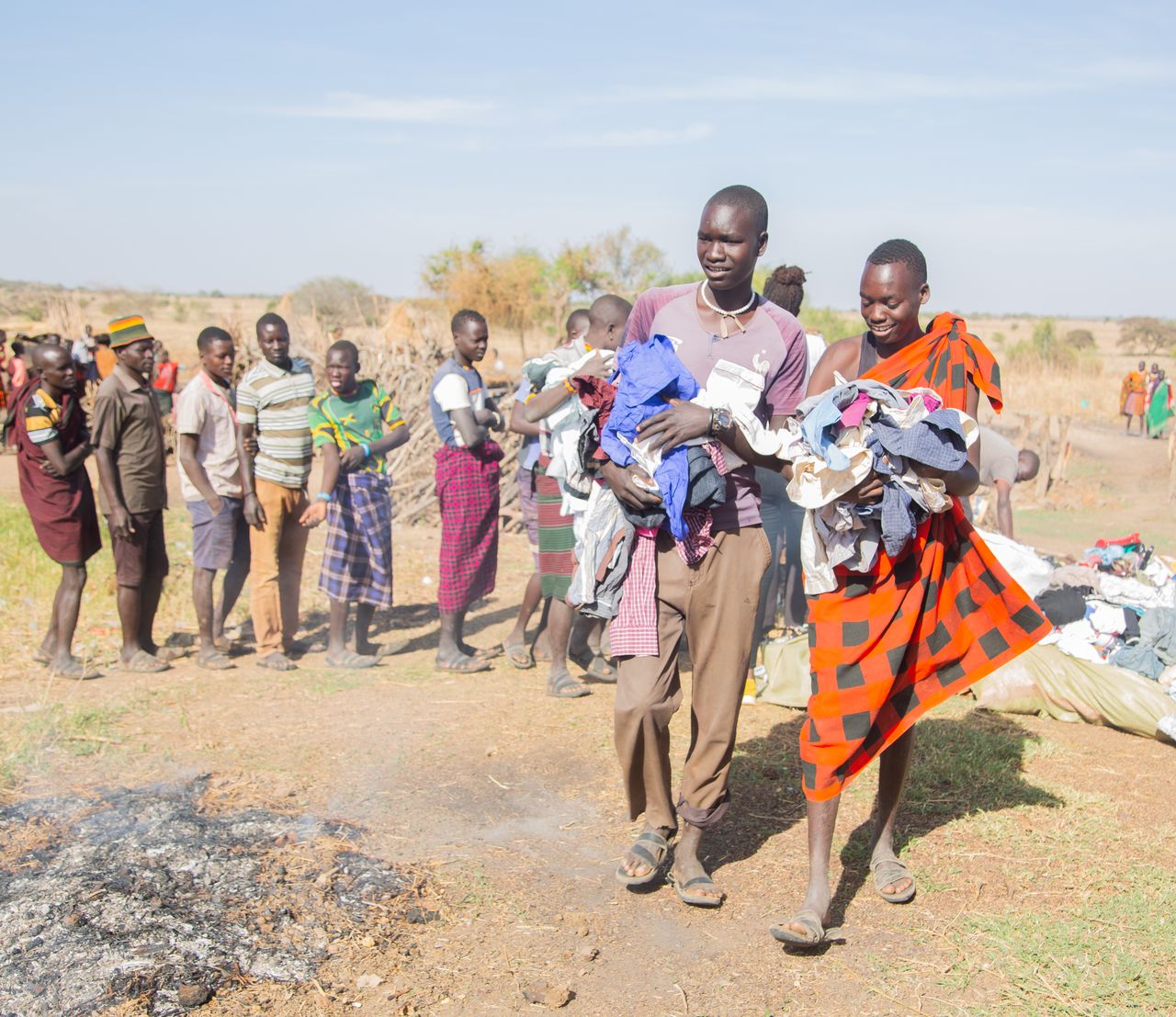 Local community members participate in a clothing distribution event under sunny skies in a rural setting.